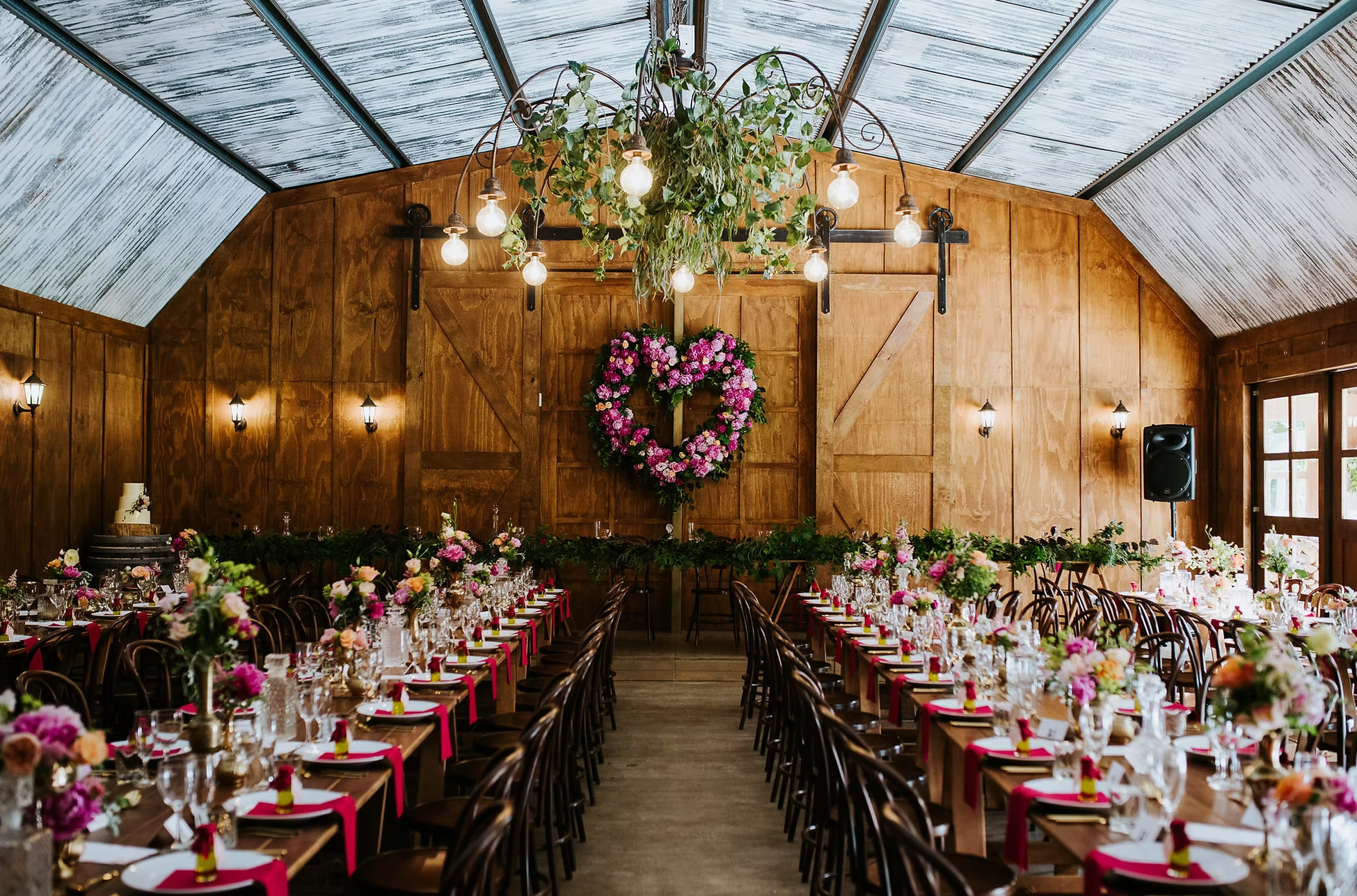 a large wood panelled dining room which is a converted barn with styled tables, flowers and colourful decor. A heart shaped flower wreath is also on the wall