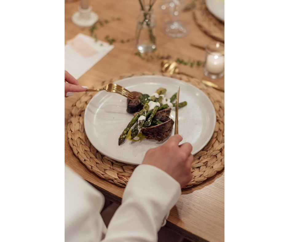 Person about to eat a dish of meat and asparagus on a white plate with gold cutlery.