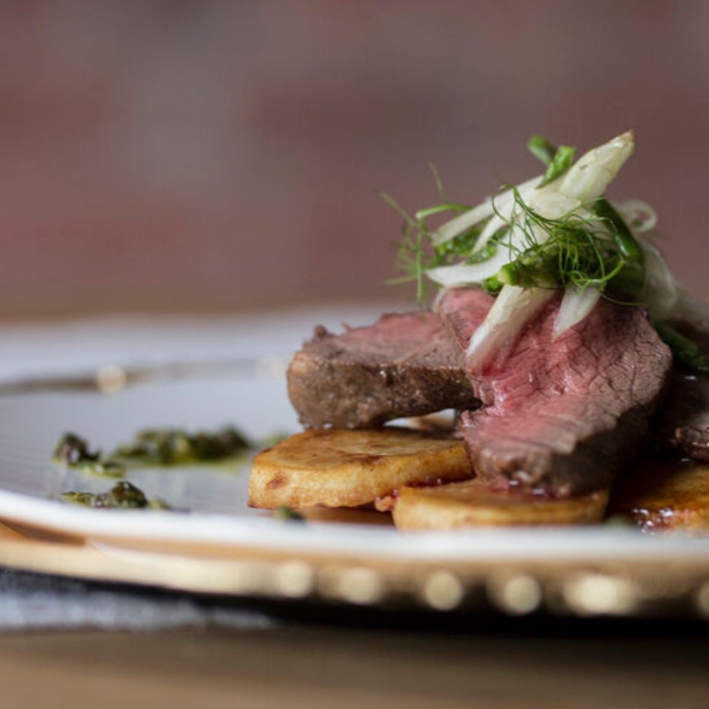Plated dish with sliced beef, potatoes, and garnishes on a wooden board.