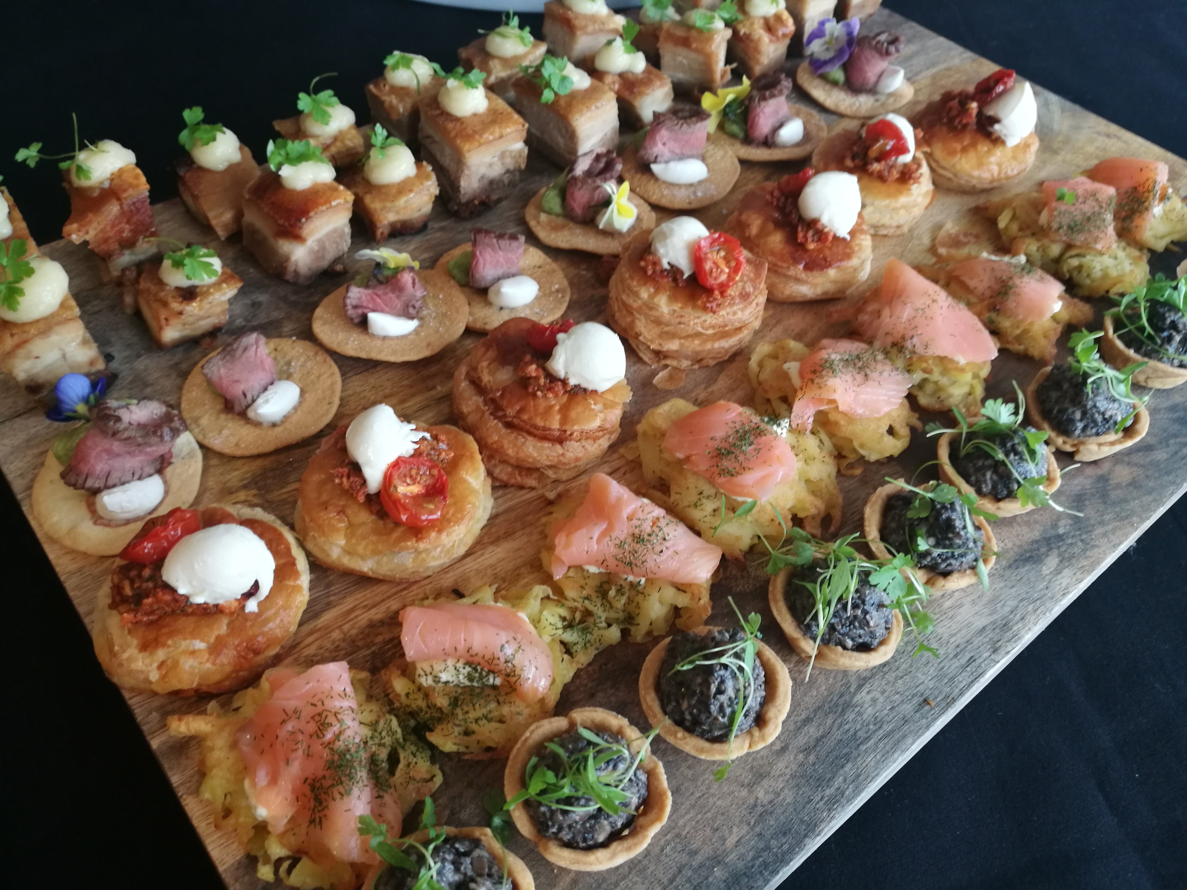 Assorted canapés on a wooden board with a dark background