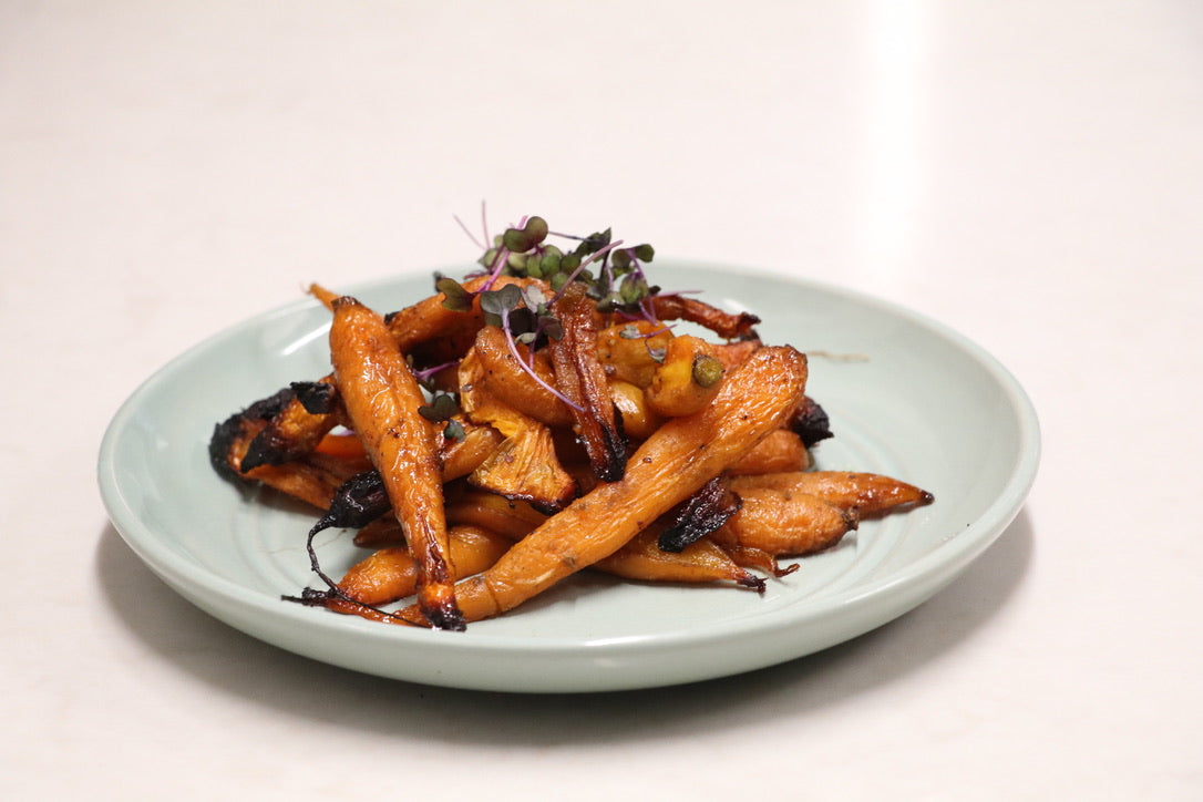 Cooked Honey roasted  baby Carrots. Presented on light blue dish with micro green garnish