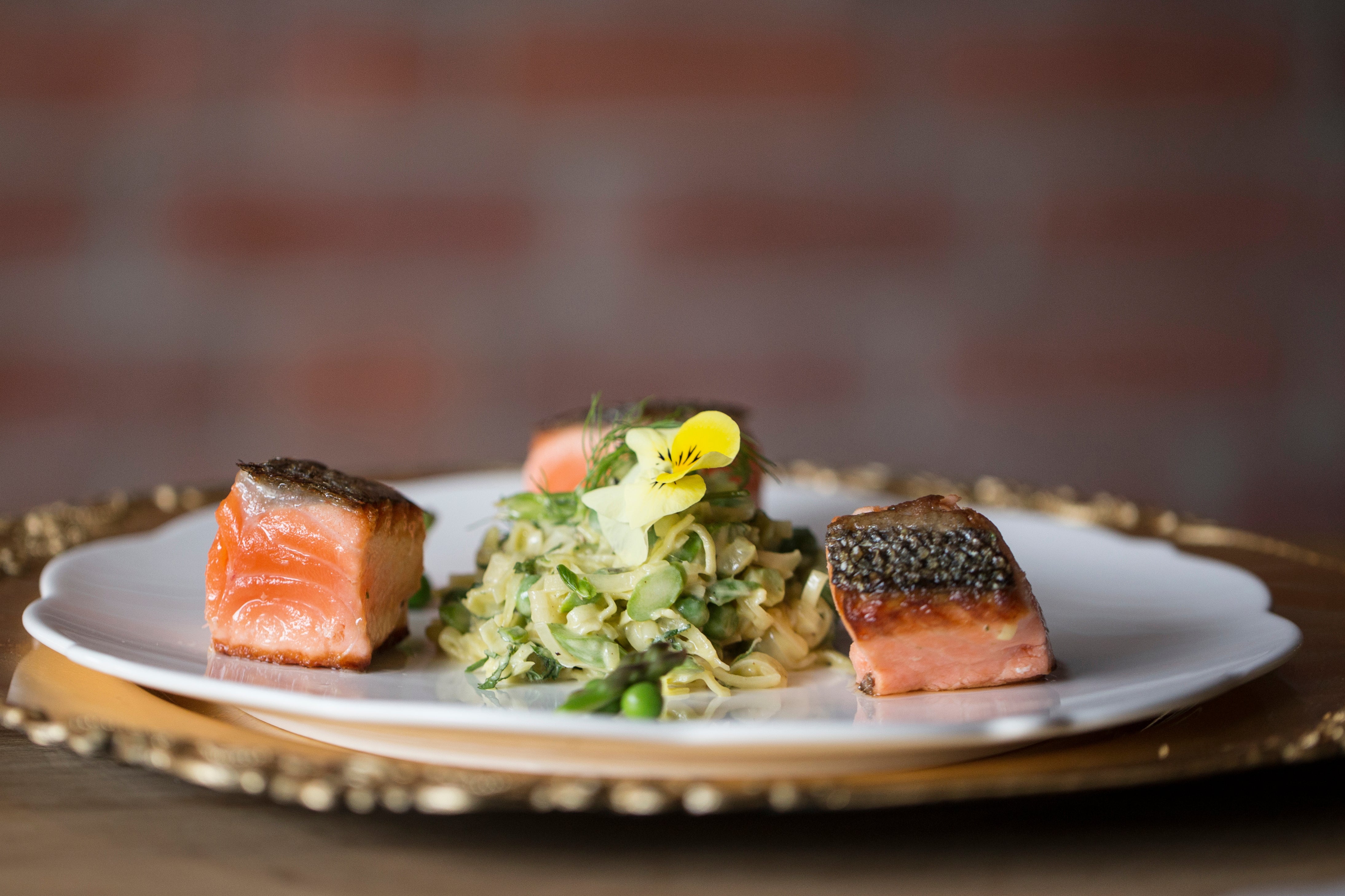 Plated dish with salmon and salad on a wooden table with a blurred brick wall background