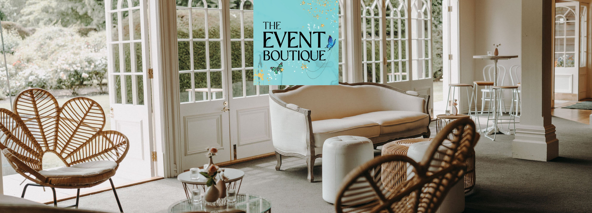 Bright, airy event space with elegant vintage-style sofa, rattan chairs, and floral decor, set up for a boutique gathering