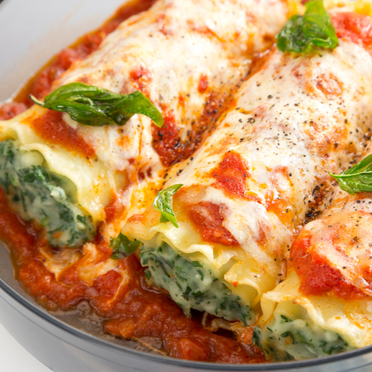 Spinach lasagna roll-ups with tomato sauce and cheese in a glass dish on a white background